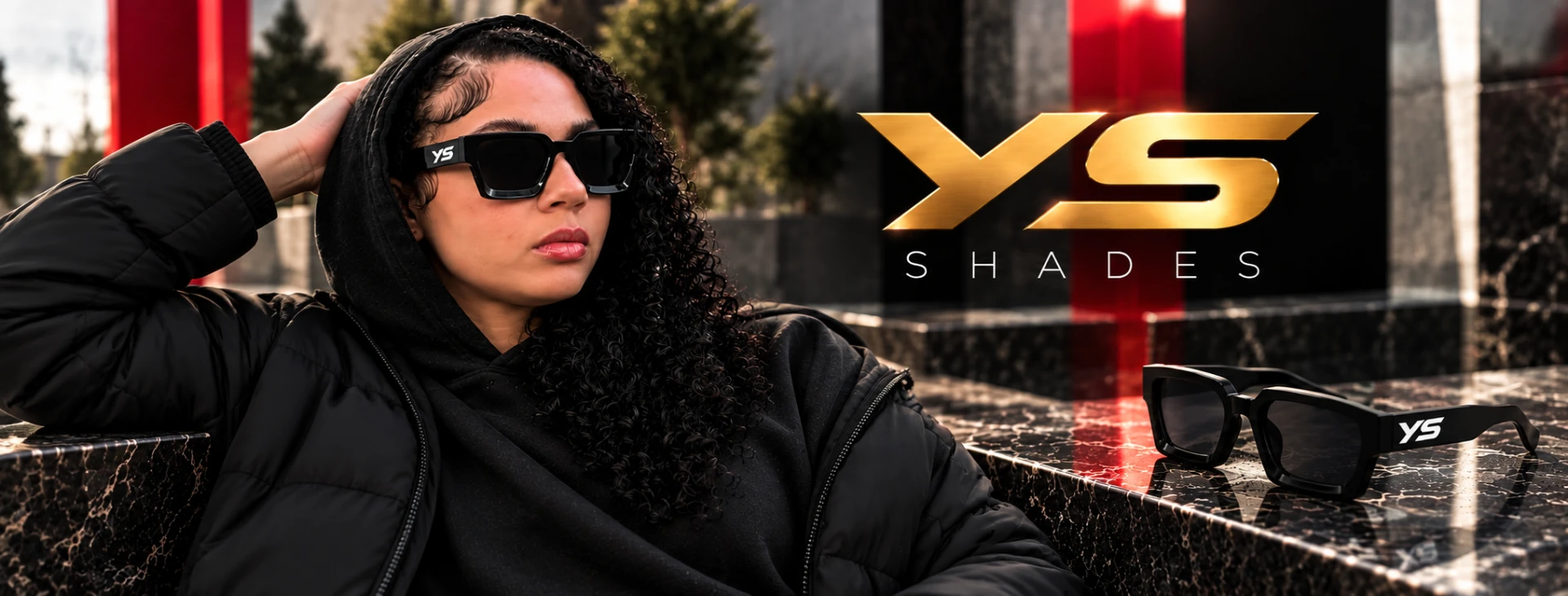 YS Shades — a model in a black hoodie and black YS sunglasses beside a pair of shades resting on dark marble, under the gold YS Shades logo